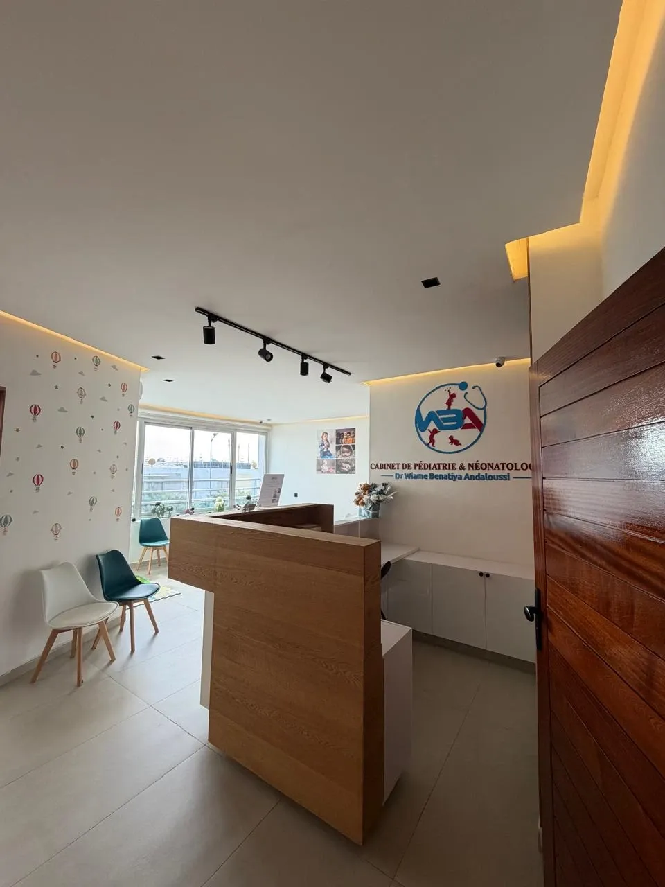 Accueil du cabinet : comptoir en bois clair, logo WBA au mur et coin d’attente décoré pour les enfants