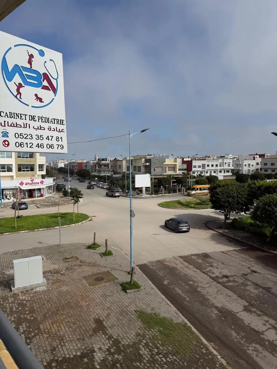Vue depuis le cabinet sur le rond-point, avec l’enseigne du cabinet et la boutique Shahine en face
